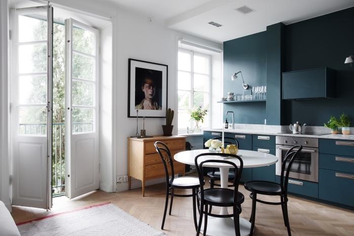 Nordijski dekor, kuhinja s temno modrim pohištvom in stenskimi policami, bela jedilna miza s črnimi stoli