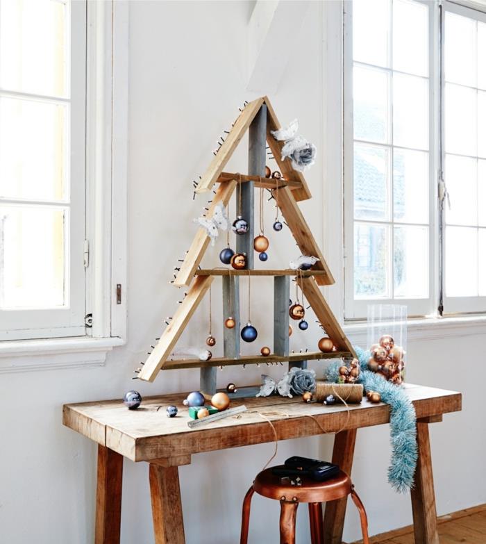 medinė eglutė, padaryta iš padėklų, oranžinės ir mėlynos spalvos dekoratyviniai Kalėdų rutuliai, varinė apdailos taburetė, mėlyna girlianda