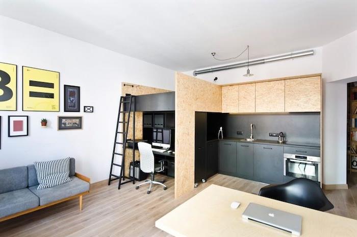 Skandinaviško stiliaus juoda ir medinė virtuvė su rašomuoju stalu ir miegamojo zona virš miegamojo, atsiverianti į minimalistinio dizaino svetainę