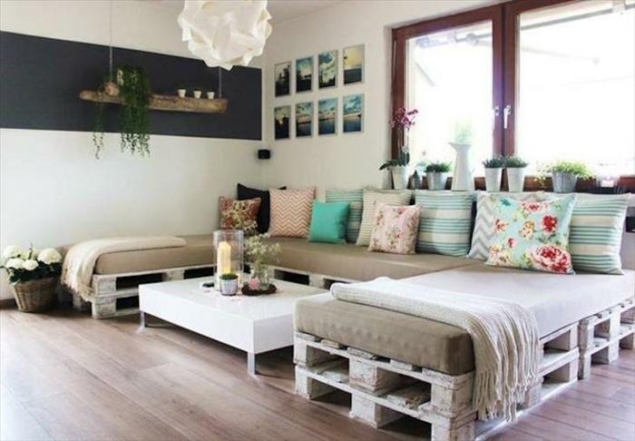padėklų sofa, panaši į c, padengta smėlio spalvos putų čiužiniais ir dekoruota daugybe pagalvių, įvairių dydžių ir spalvų