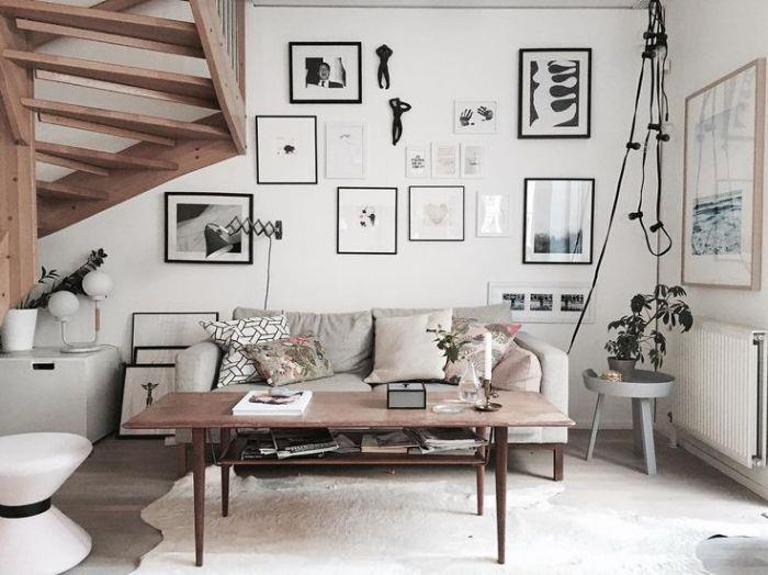 juodai balti deko rėmai ant baltos sienos senovinė medinė kavos staliuko sofa perkrauta dekoratyvinėmis pagalvėlėmis mediniai laiptai