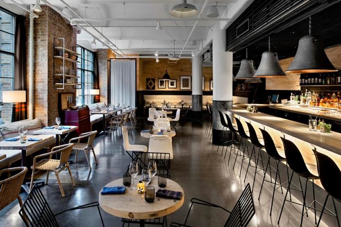 graži pramoninio palėpės stiliaus kavinė, kabančios lempos, nedideli kvadratiniai stalai, baltos lubos, juodos baro kėdės