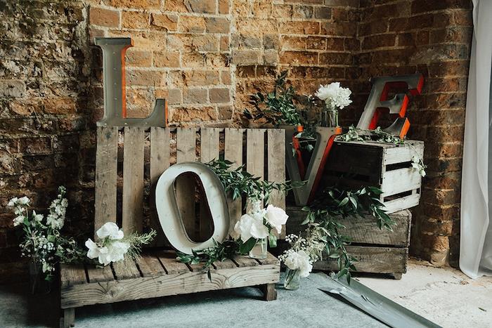 dekoratyvinių medinių dėžių ir kaimiškų medinių padėklų idėja, meilės didžiosios raidės, žalios girliandos ir baltos gėlės, kaimiškos prašmatnios vestuvės