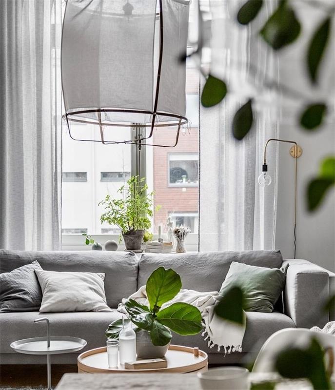 šviesiai pilka sofa medinis kavos staliukas baltos užuolaidos dideli langai jaukioje, prašmatnioje skandinaviškoje svetainėje