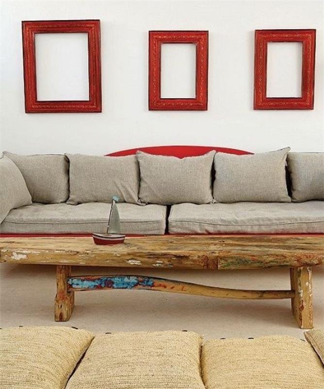 okrasite belo steno z rdečimi okvirji v različnih oblikah, sivim in rdečim kavčem, mizo iz surovega lesa, blazinami na tleh, rjavo preprogo