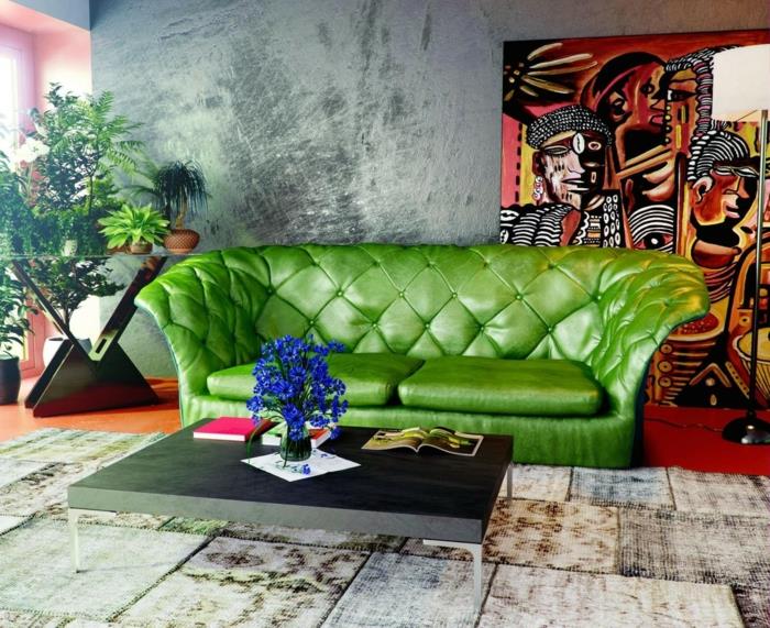 voščena betonska stenska dekoracija, večbarvna stenska plošča v sijočih barvah, zelen kavč, patchwork preproga, sodobna mizica