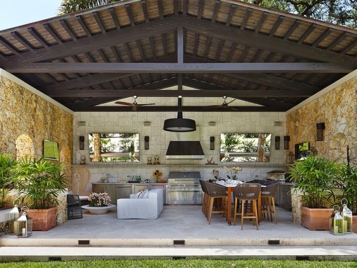 modelio virtuvė sode su tamsiu medžio masyvo stogu ir akmeninėmis sienomis, sodo baldai su balta sofa