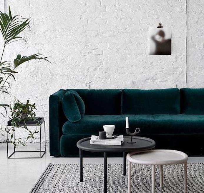benzininės mėlynos sofos idėja, balta plytų siena, pramoninis stilius, pilkas kilimas, juodas ir medinis stalas, juodas naktinis stalas, žalias augalas