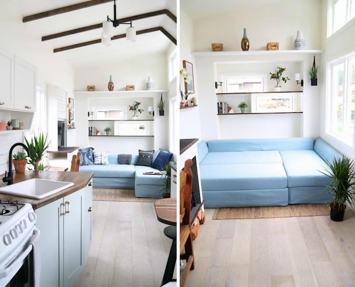 modulinės dizaino sofa ir dvigulė lova mėlynos spalvos, baltos sienos, mažos atviros rudos sijos, atviros lentynos, miniatiūrinė medžio ir mėlynos spalvos virtuvė