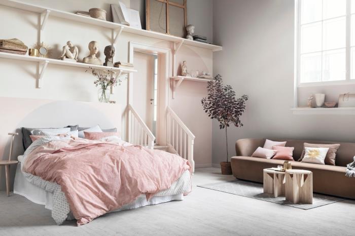 studijos išdėstymas su šviesiai rožiniais ir smėlio spalvos dažais, sieninė saugykla su medinėmis lentynomis, rudos sofos modelis su kavos staliuku