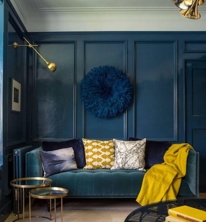 rumeni poudarki za peps brez dnevne sobe, oblečeni v modro z modrim kavčem iz zelenih, pisanih okrasnih blazin, parketa iz svetlega lesa, peresne stenske dekoracije