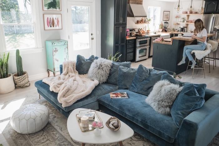 didelė jauki anties mėlyno aksomo sofa, esanti elegantiškos bohemiškos svetainės centre, atvirame virtuvėje