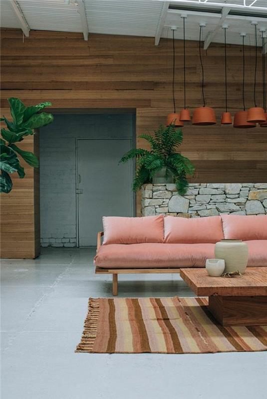 lašišos rožinės spalvos sofa sofos rudos spalvos kilimas su smėlio spalvos juostelėmis rudos vaškuotos betono grindys