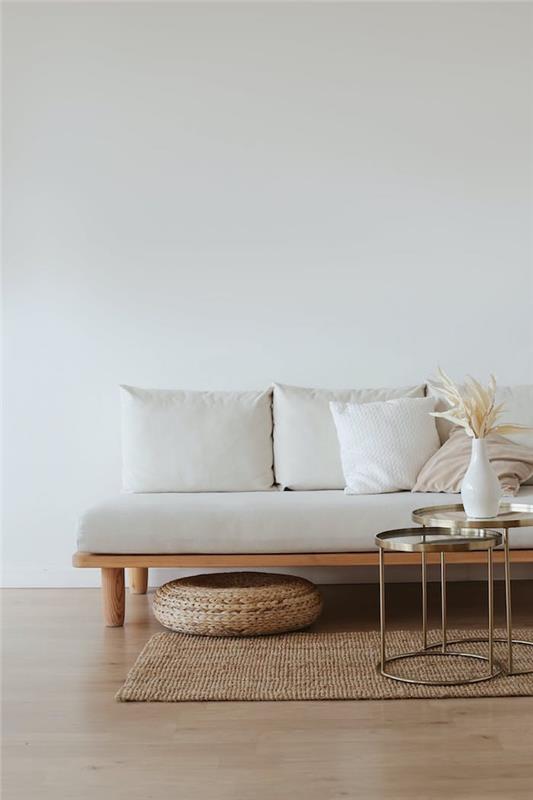 kokybiška sofa iš balto ir medinio pagrindo, viename sofos gale metalinis smėlio spalvos kilimas