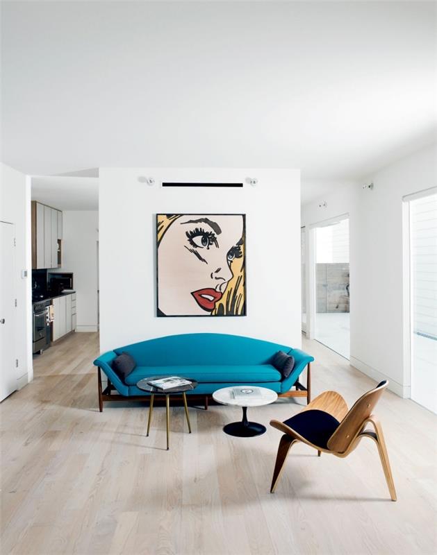 Orijinal bir pop art resmiyle ilişkilendirilen ve küçük siyah noktalarla yüceltilen ördek mavisi kanepe, bu kusursuz beyaz oturma odasında merkezi bir unsur haline geliyor.