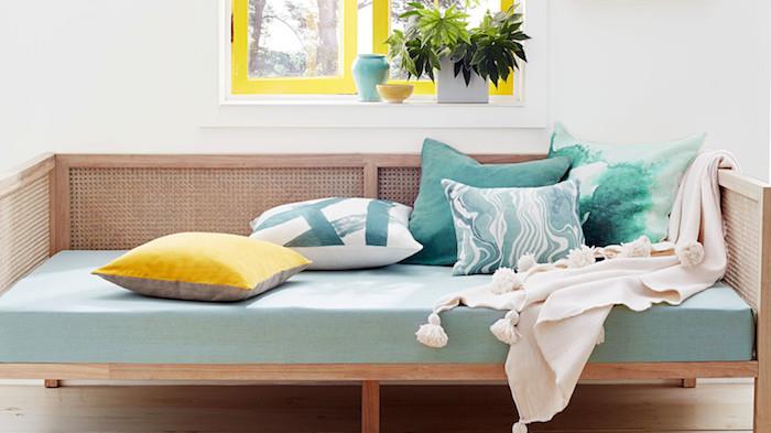 lesena zofa z žimnico v barvi celadon, okrašena z blazinami, modra, zelena in rumena, svetlo siva prevleka, okna z rumenimi okvirji, stena v belem ozadju