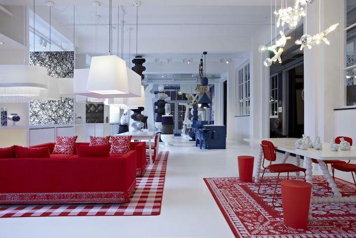 dizaino raudona sofa svetainėje, atvira virtuvei, valgomasis, baltos sienos ir grindys, mėlyna valgomojo zona, originalūs pakabinami žibintai