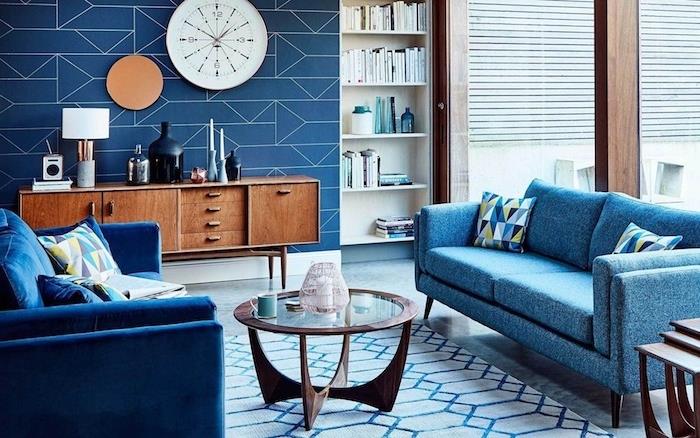 modre zofe v modro -beli dnevni sobi, lesena in steklena mizica, bela ura, lesena TV omara, bela in modra preproga