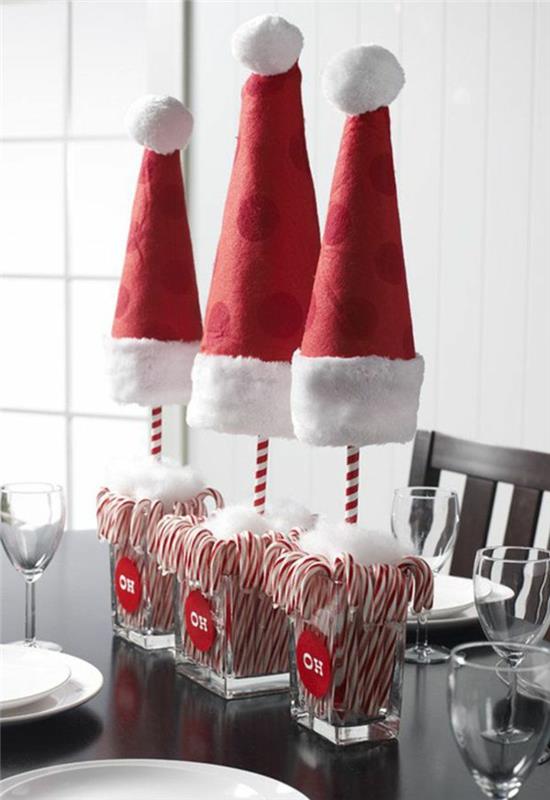 Centrotavola con dei bicchieri di vetro e caramelle all'interno, cappucci di Babbo Natale di feltro rosso