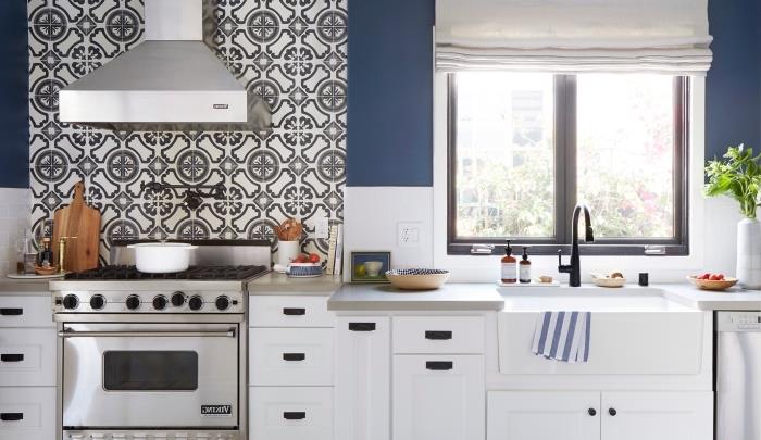 bele ploščice, stensko barvanje v kuhinji v beli in temno modri barvi, belo pobarvano leseno kuhinjsko pohištvo s črnimi ročaji