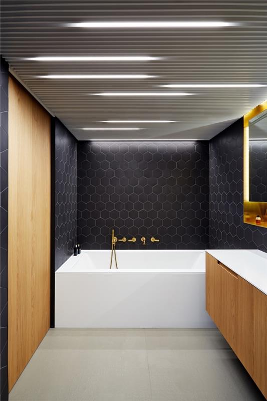 ilgas vonios kambario išdėstymas, modernus juodos ir medinės spalvos vonios kambarys su balta vonia ir smėlio spalvos grindimis