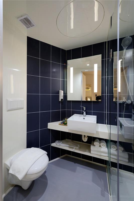 PVC duvar kaplamasını parlak kaplama ve koyu mavi geniş formatlı karolarla birleştiren küçük banyo
