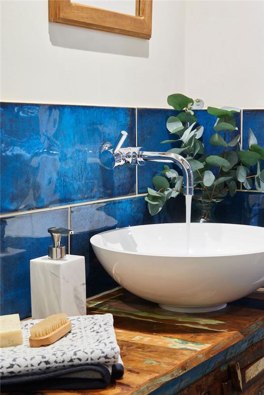 bel umivalnik na delovni plošči iz surovega lesa, kopalnica z modrimi ploščicami, bela stena, modra pantone elegantna kopalnica