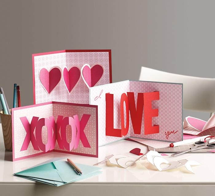 3 d pop -up kortelė iš popieriaus, xo raštas, rausvos ir raudonos spalvos žodžiai meilė ir širdys rožiniame fone, mėlyni vokai