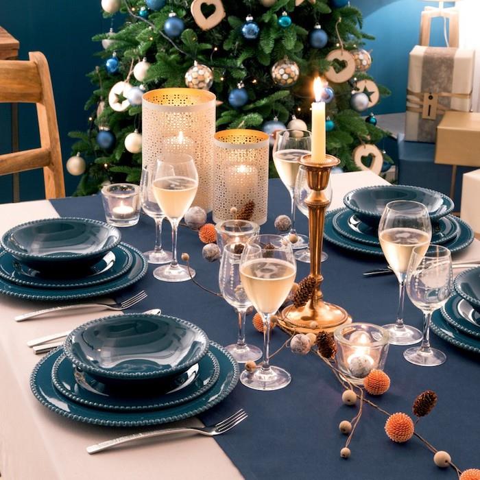 elegantna novoletna dekoracija za zabavo z modrim tekačem za mizo in modrimi krožniki, zlato svečo, cvetličnim središčem, originalnimi svečniki