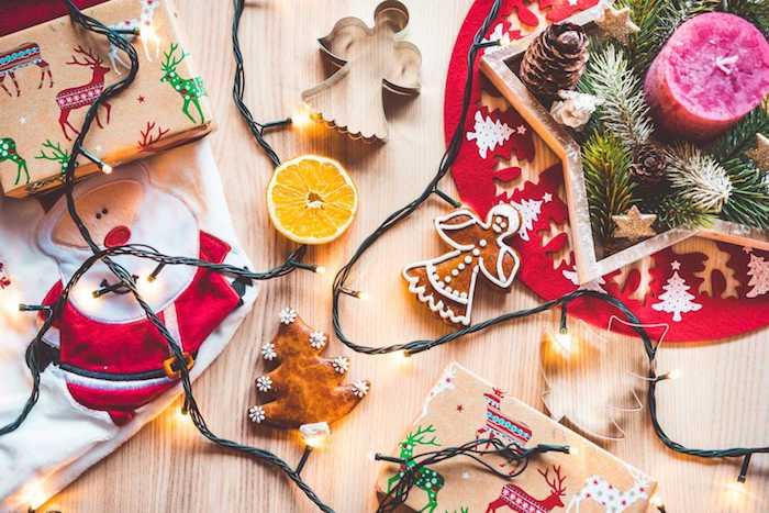 Kalėdiniai tapetai, Kalėdų stalo centras iš medžio žvaigždės su šakomis ir kankorėžiais bei rožine žvake viduje, šviesi girlianda, sausainiai ir dovanos, supakuotos į amatų popierių su šventiniais raštais