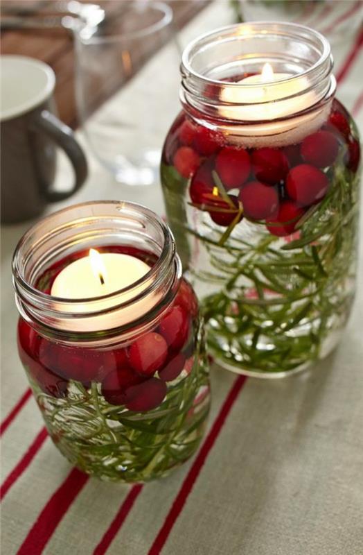Božična obrt s steklenimi kozarci za marmelado, napolnjena z vodo z okusom, jelkinimi listi in šipki, z okroglo belo svečo na vrhu