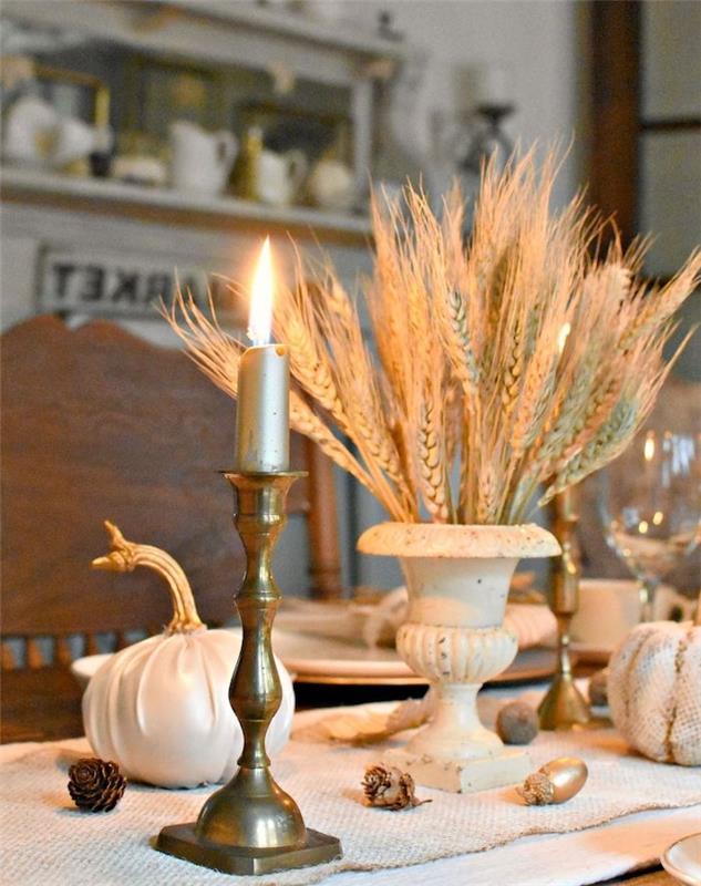 zlati svečnik in pšenični klasji za okrasitev tekača na mizi z borovci in bučami, oblečenimi v tkanino