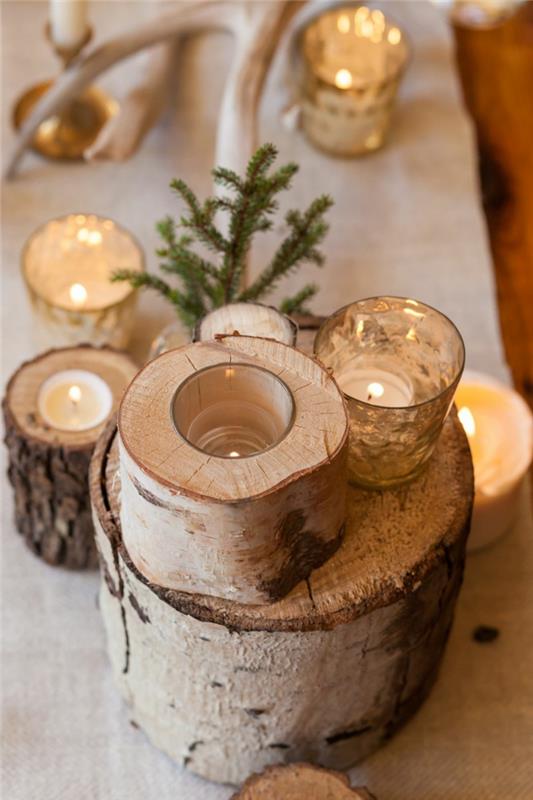 namizna dekoracija za božič v lesenih deblih, prižgane sveče, zelena vejica bora, osrednji del