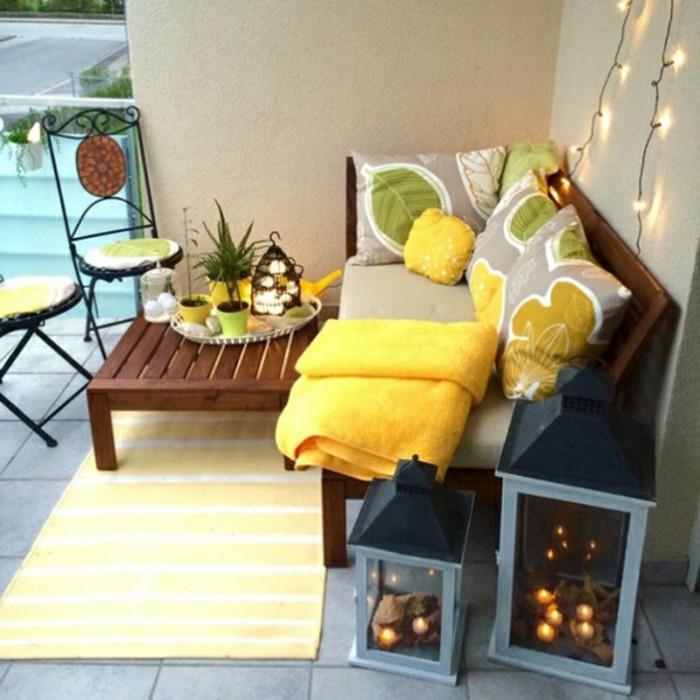 ideja rjave lesene mize in kavča s sivo dekoracijo sedežnih blazin in sivimi, rumenimi in zelenimi okrasnimi blazinami, rumeno preprogo, okrasnimi lučkami