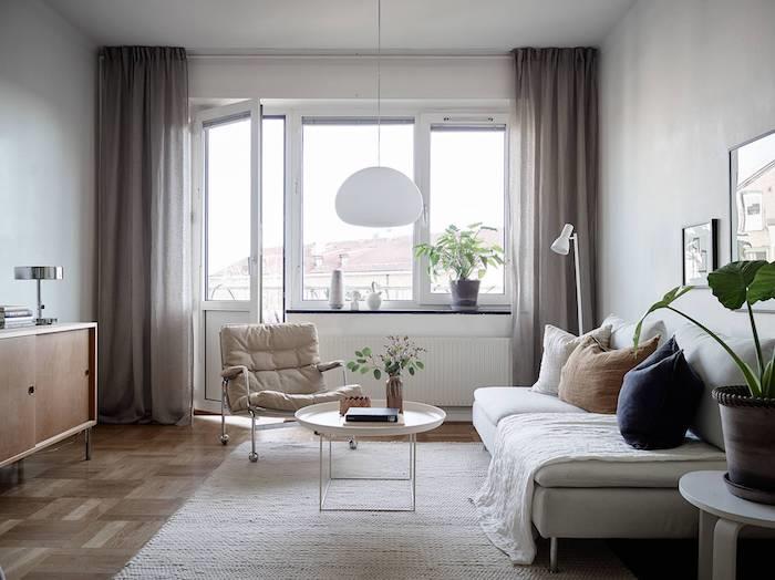 sivo -beli model dnevne sobe s svetlo sivim kavčem, svetlo rjav parket, okrogla klubska mizica, ležalnik v sivi barvi, skandinavski slog lanene zavese v svetlo sivi barvi