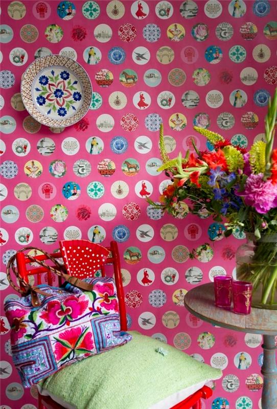 ryškus interjero dizainas su rožiniais gėlių tapetais su įvairiais įvairiaspalviais raštais, dekoru su senoviniu apvaliu stalu ir raudona medine kėdė