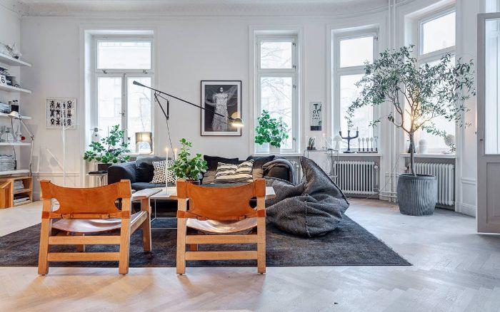 medinės kėdės, kurios sušildo atmosferą šiltai pilkoje ir baltoje gyvenamojoje patalpoje su gulinčiomis sėdynėmis ir kai kuriais patalpų žaliais augalais