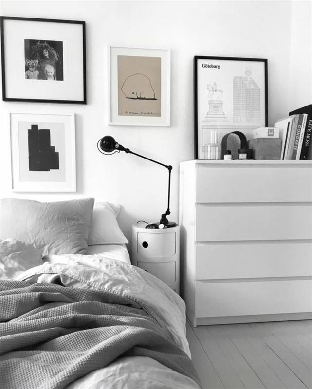 modernus miegamojo dekoras, didelė balta laikymo spintelė, mažas baltas naktinis stalas ir žibintas, įrėminti paveikslai