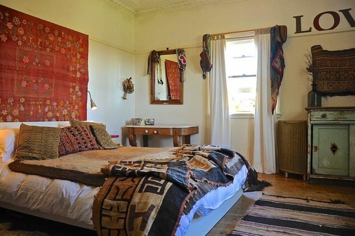 postelja v slogu boho chic, rdeča viseča stena, pravokotno ogledalo, majhna omamljena modra omara