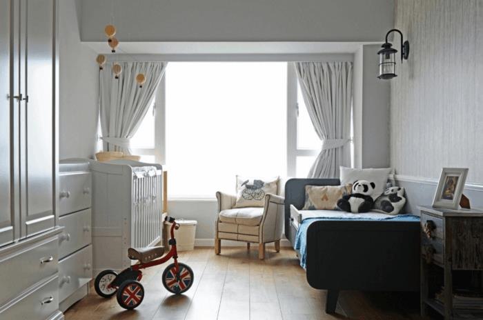 zavese v svetlo sivi barvi, trikolesno kolo, 2-letna otroška postelja, tla iz deske, kremni naslanjač, ​​stenska luč