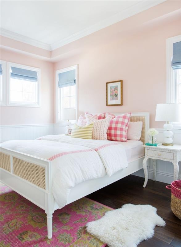 pastel boya toz pembe duvarları, beyaz ahşap çerçeveli koza yatak dekorasyonu ve dekoratif minderleri olan bir yatak odası örneği