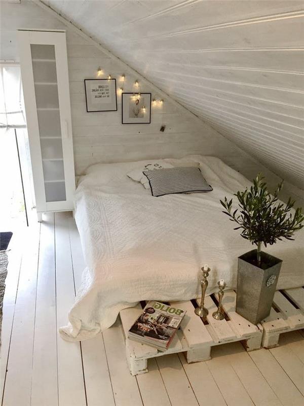 beyaza boyanmış alçak bir palet yatağı ile tamamen beyaz tek renkli bir çatı katı yatak odası düzeni