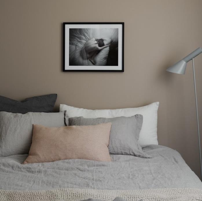 lahka taupe spalnica, sivo, belo in bež posteljnina, stena okrašena s črno -belo risbo, siva svetilka