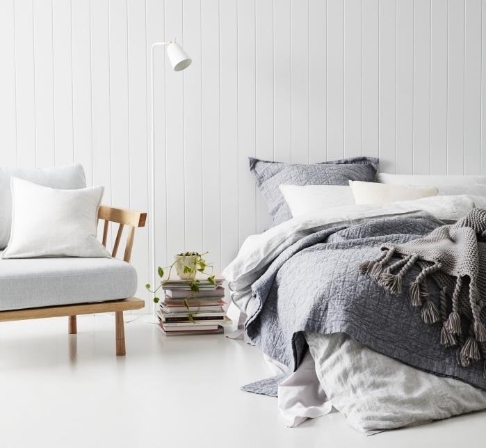 model spalnice za odrasle z zapečkanjem z belo talno in stensko oblogo, lesen naslanjač z belo sedežno blazino, belo in sivo posteljnino, kup knjig