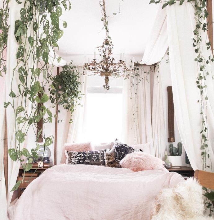 spalnica za odrasle, kokosova posteljnina, bele, črne in roza blazine, postelja z baldahinom in plezalne rastline, eleganten lestenec