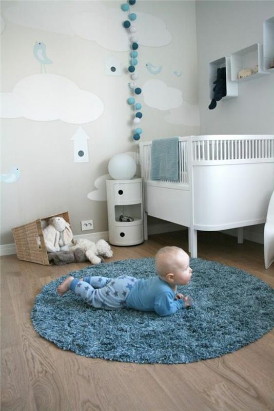 odanın ortasında ördek mavisi renginde yuvarlak halı ve beyaz ve ördek mavisi toplar şeklinde duvar dekorasyonu ile erkek bebek odası dekoru