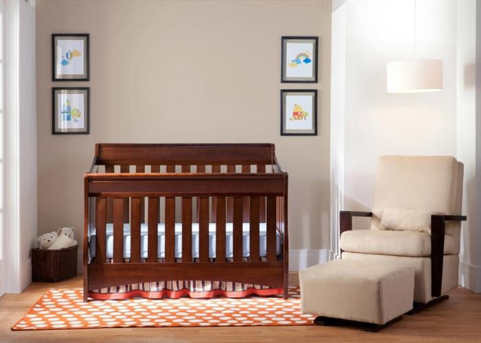 paprastas kūdikio kambarys, smėlio spalvos fotelis, medinė lova, tamsiai mėlyna siena, geometrinis kilimėlis