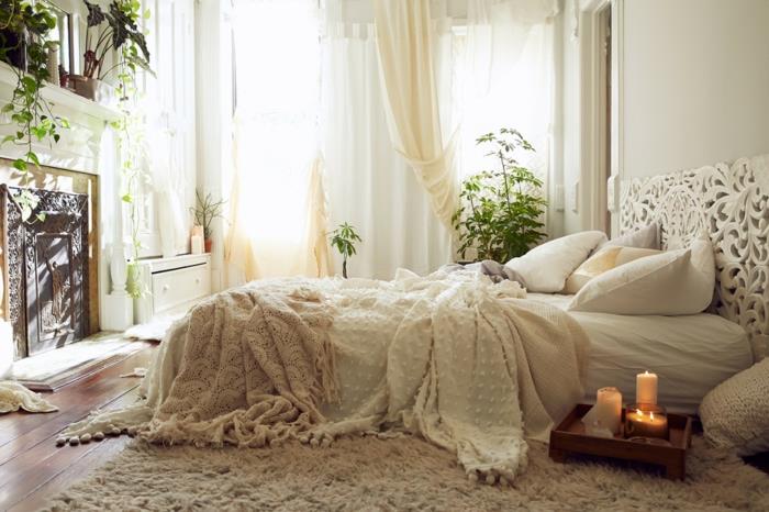 šiuolaikiška suaugusiųjų miegamojo apdaila, smėlio spalvos kilimas, kreminė lovos danga, žali augalai, baltos žvakės