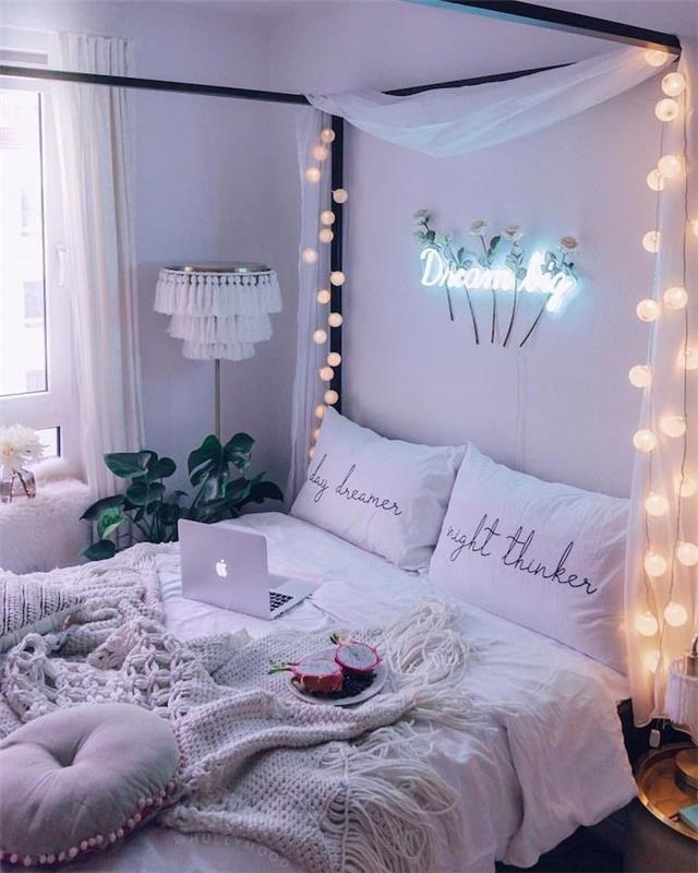 romantiška balta lova su baldakimu skandinaviškam miegamojo dekorui su baltu elito rinkiniu, šviesaus rutulio girlianda, žalias kambarinis augalas, šviesios galvūgalio neoninės raidės