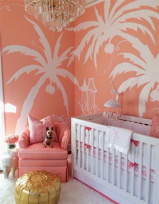 otroška soba s steno v barvi lososa, na stenah naslikane bele palme, roza naslanjač in kristalna stropna svetilka